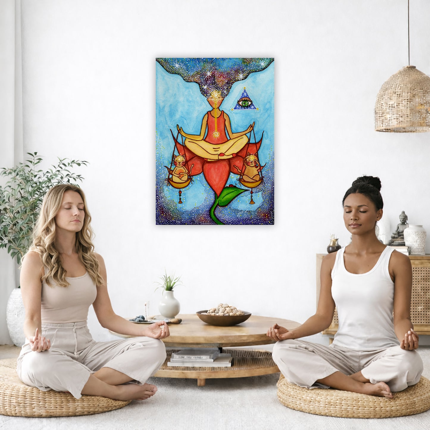 Poster of a woman meditating on a lotus with a glowing third eye and holding scales balancing two cats. This is a thumbnail of the original hand-painted watercolor by Brazilian artist Thaís Suizo for the LET'S MEDITATE SERIES of mediation guides.  The poster is in the center of the living room wall. Two women are sitting on wicker pillows meditating. Behind them is a small round coffee table with incense, a green potted plant and a bowl of shells. There is a potted plant to the left and a Buddha statue and 