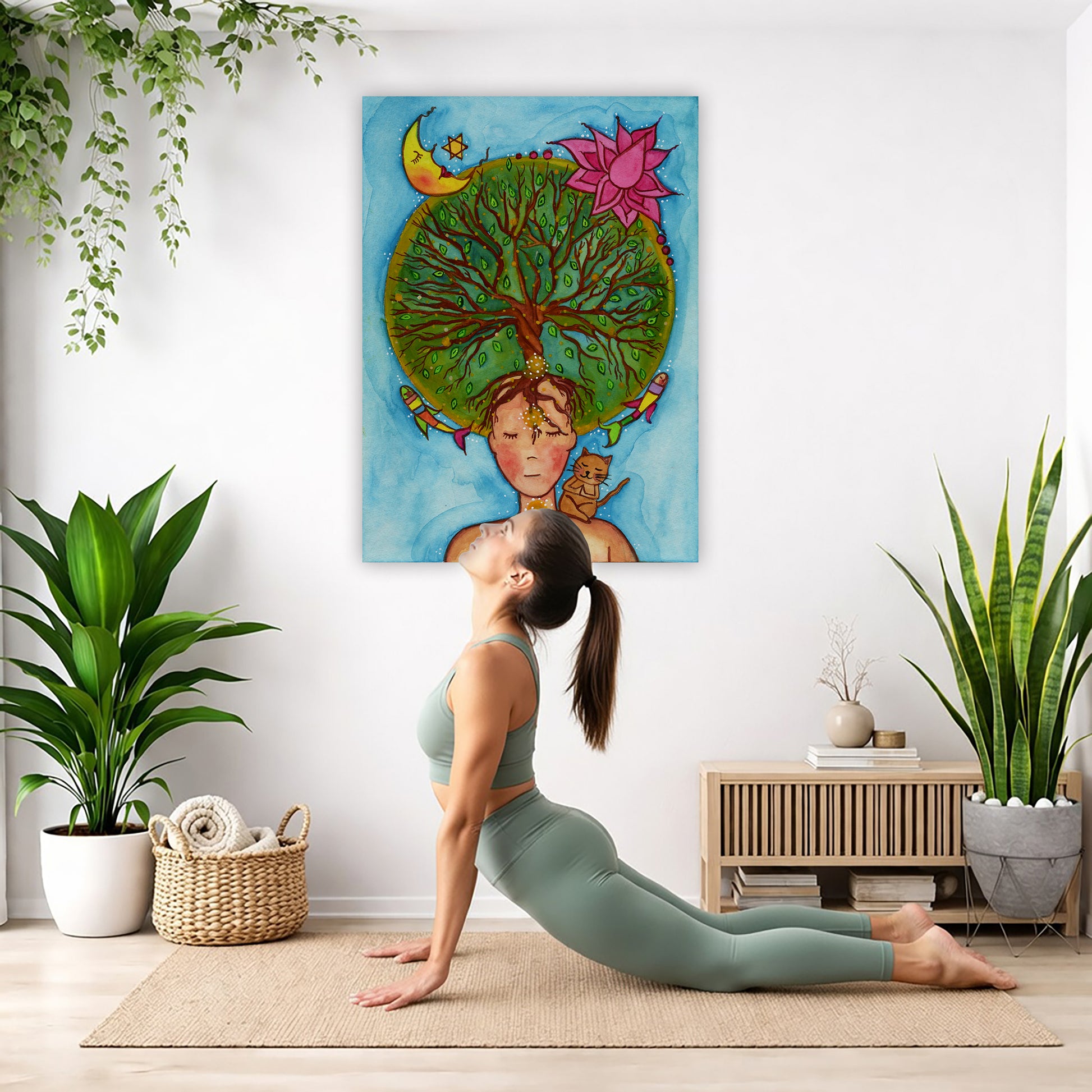canvas of a woman meditating with her crown chakra blooming into the tree of life. Her cat is sitting on her shoulder.  The poster is in the center of the living room wall. Below the poster a woman is doing the yoga posture downward facing dog on a yoga mat.