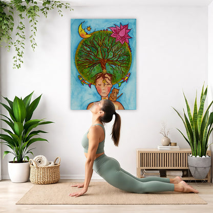 canvas of a woman meditating with her crown chakra blooming into the tree of life. Her cat is sitting on her shoulder.  The poster is in the center of the living room wall. Below the poster a woman is doing the yoga posture downward facing dog on a yoga mat.