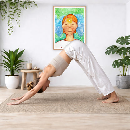 Poster of a man with a glowing brow chakra.  The poster is in the center of the living room wall. Below the poster a woman is doing the yoga posture downward facing dog on a yoga mat.