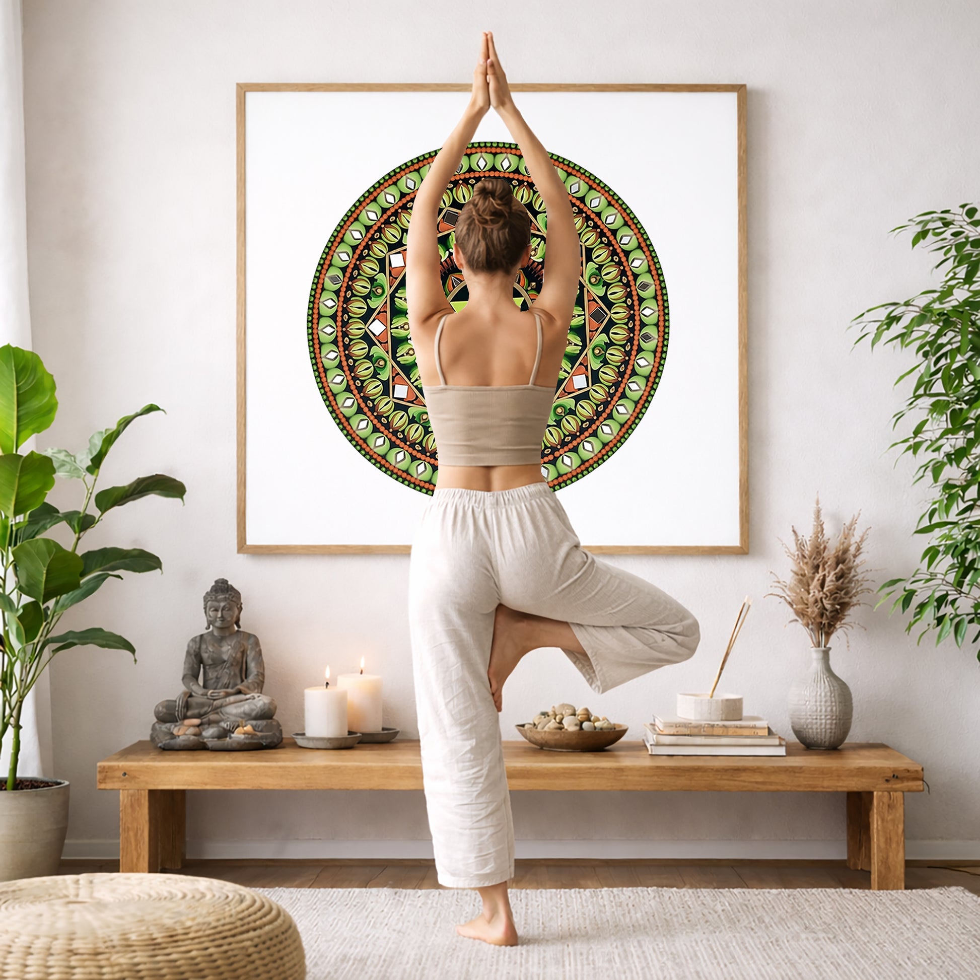 Mandala with a green star shape at the center surrounded by detailed symmetrical patterns, meditation artwork printed on a poster. The mandala is framed hanging on a living room wall. A woman is doing the yoga tree pose (Vrksasana) facing the mandala. There is a coffee table in front of her with candles and a Buddha statue. There are green potted plants on each side of the room.
