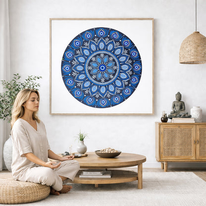 Blue mandala poster featuring intricate circular sacred geometry in deep navy and layered blue tones, detailed dotwork pattern designed for meditation spaces, yoga rooms, and calming wall decor.  The mandala poster is framed and is in the center of the living room wall. A woman is on a chair on the left side of his living room meditating. There is a green potted plant behind her. On the right side is a cabinet with a Buddha statue on it. 