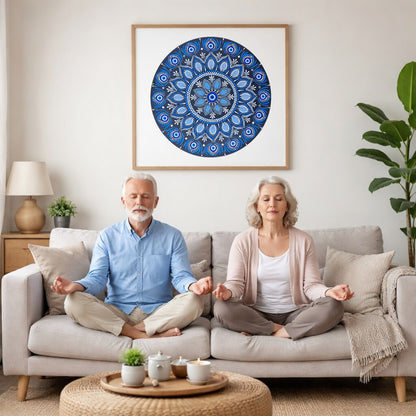 Blue mandala poster featuring intricate circular sacred geometry in deep navy and layered blue tones, detailed dotwork pattern designed for meditation spaces, yoga rooms, and calming wall decor.  A couple is meditating on their couch. The mandala is framed on a wall behind them. There is a coffee table in front with candles burning and a potted plant. There is a potted plant to the right and shelves on the left.
