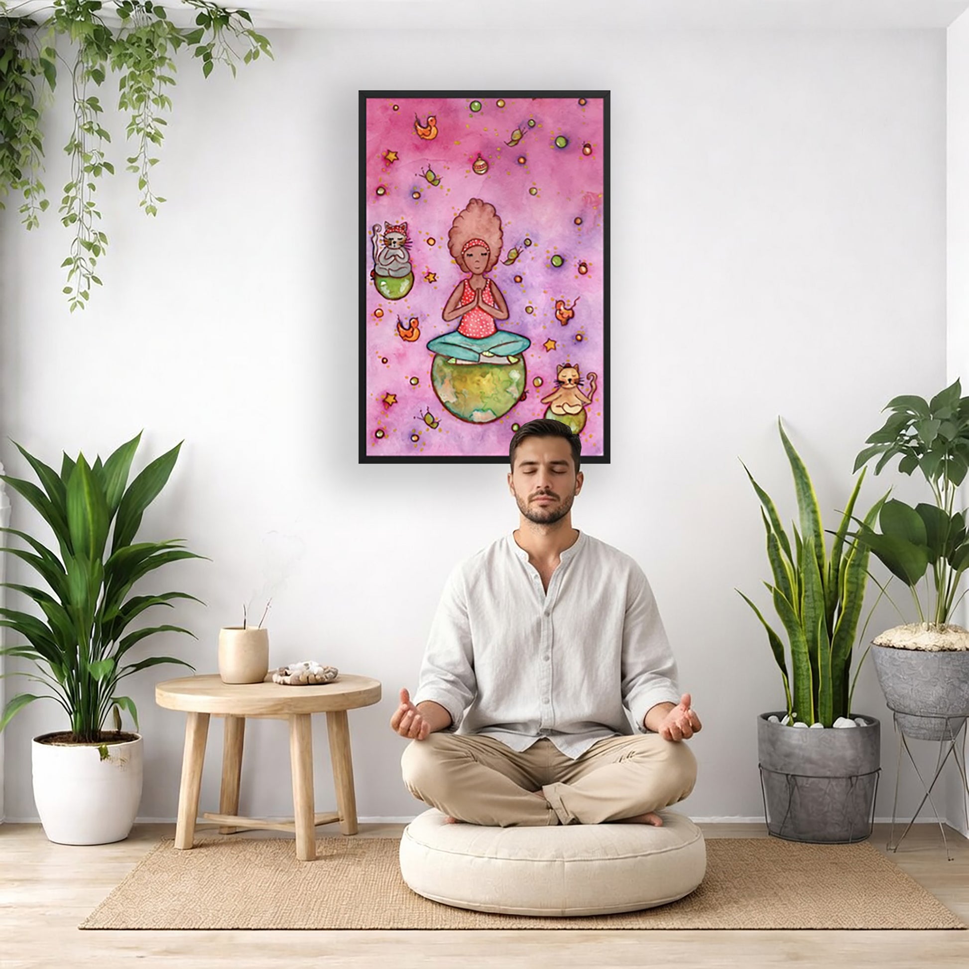 Poster of a woman and her cats meditating atop their own personal worlds with a pink background. The poster is framed and is in the center of the living room wall. There is a man meditating facing away from the wall. Behind him is a coffee table with incense and a Buddha statue. There are potted plants on the right and left side of the background.
