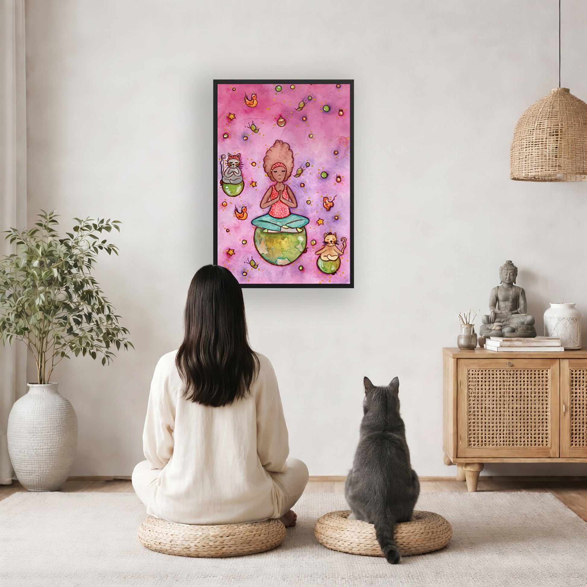 Poster of a woman and her cats meditating atop their own personal worlds with a pink background. The poster is framed and is in the center of the living room wall. A woman and a cat are staring up at the poster. There is a potted plant on the left side and a cabinet with a Buddha statue, books and incense on the right side.
