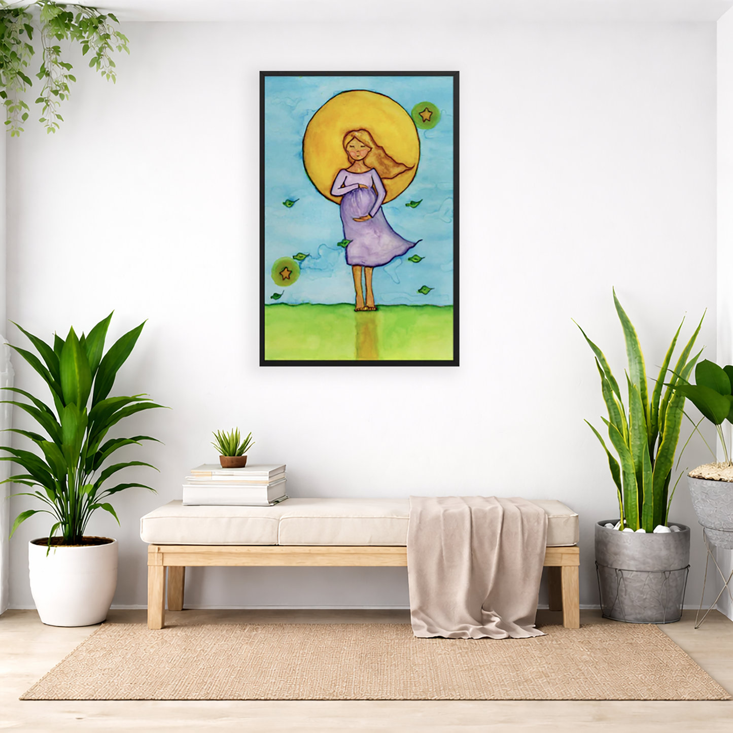 Woman standing in meditation under a bright sun with soft blue sky background, framed watercolor print.  The poster is framed and is in the center of the living room wall. Below the poster is a padded bench. On the bench is a pile of books and a small green potted plant. There is a silk sheet draped over the bench. There is a green hanging plant and floor plant on the left. There are two floor plants on the right.
