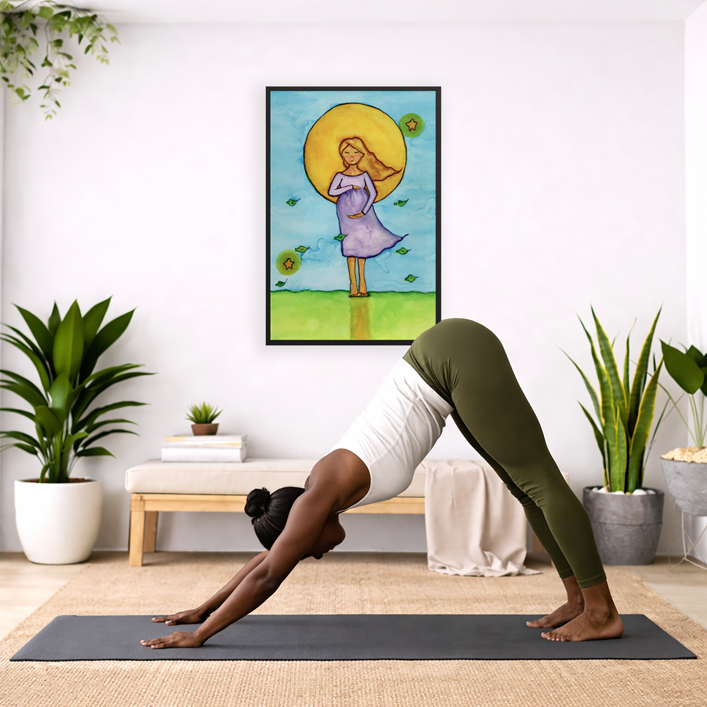 Woman standing in meditation under a bright sun with soft blue sky background, framed watercolor print.  The poster is framed and is in the center of the living room wall. Below the poster a woman is doing the yoga posture downward facing dog on a  yoga mat.
