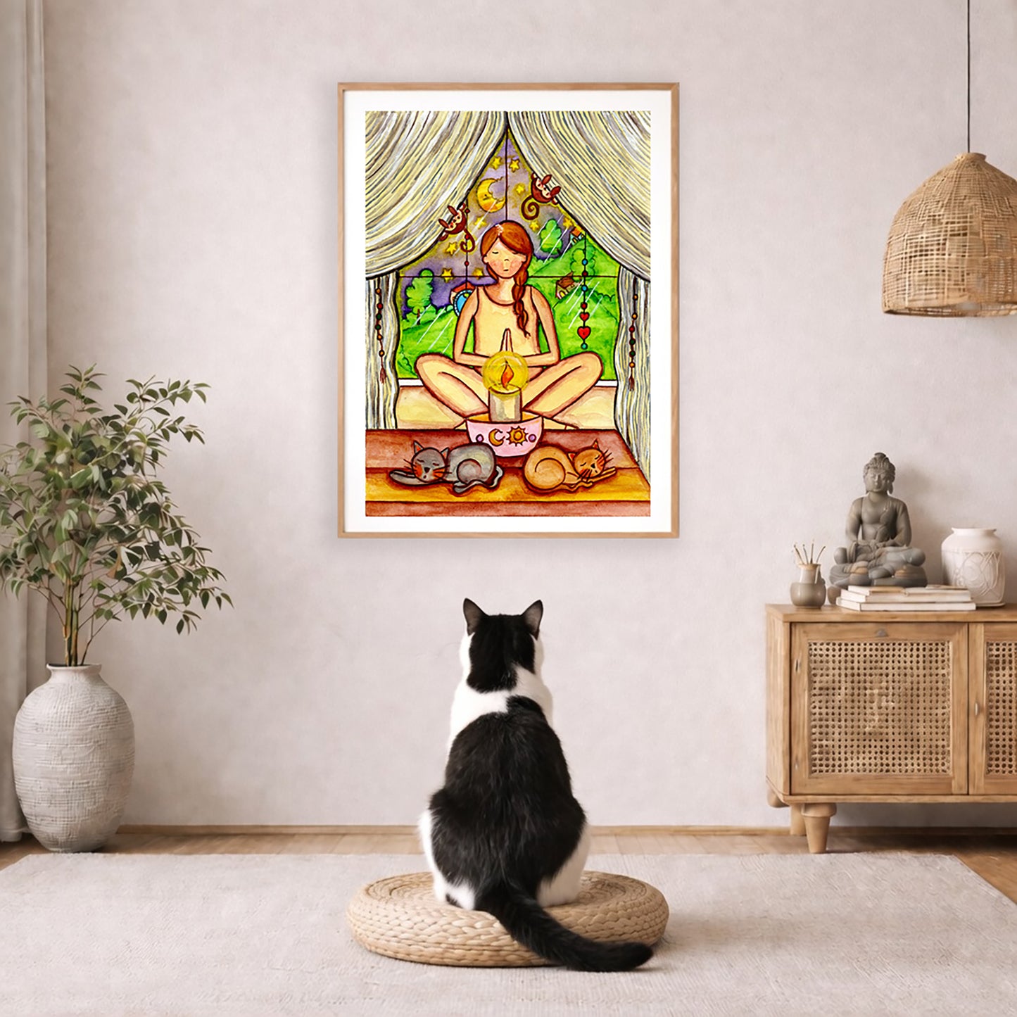 Candlelight trataka meditation design on mindfulness poster.  The poster is framed and is in the center of the living room wall. A black and white cat is staring at the poster. There is a potted plant on the left side and a cabinet with a Buddha statue on it on the right side. 
