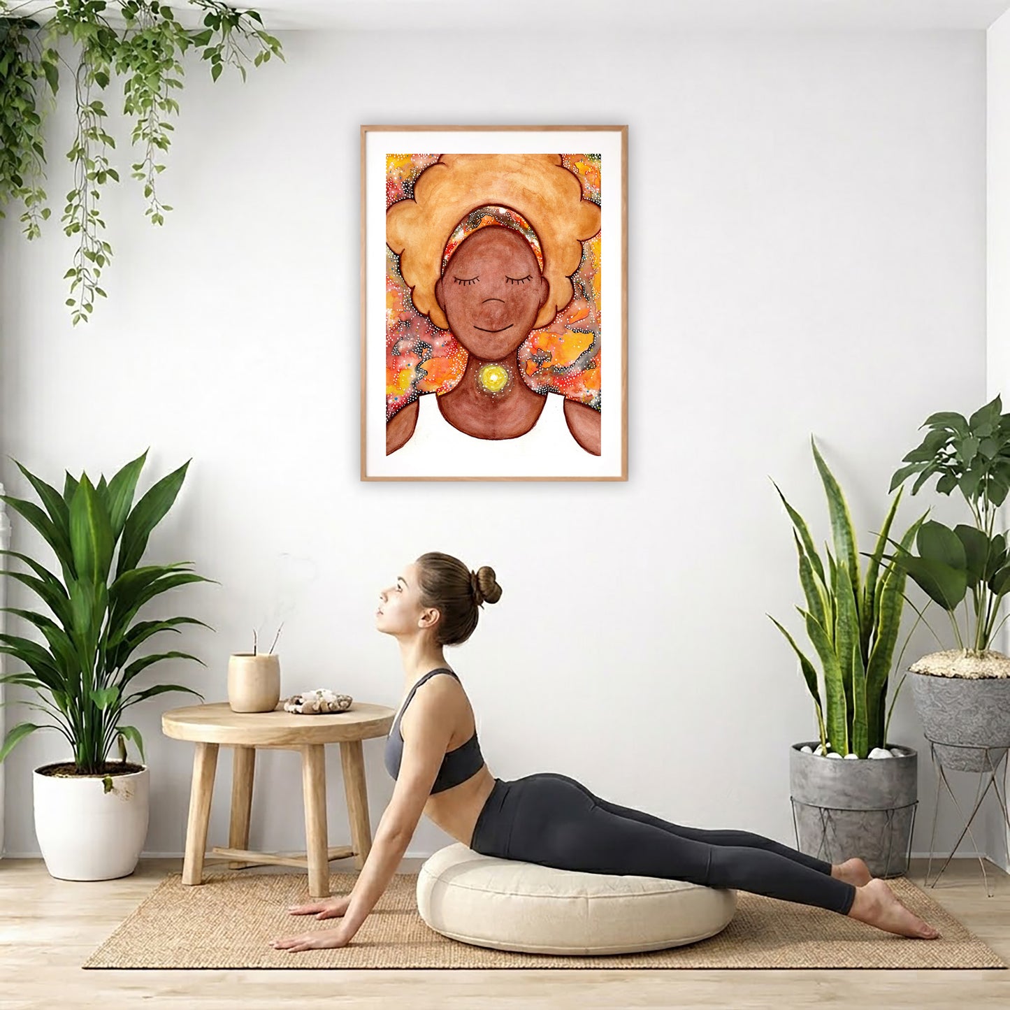 Poster of a woman's throat chakra energy glowing.  The poster is hanging on the wall. A woman on her yoga pillow is doing the cobra pose in front of the poster. There are several potted plants behind her including a hanging plant on the left side. There is a small table to the woman's left with incense and a bowl of shells on it.