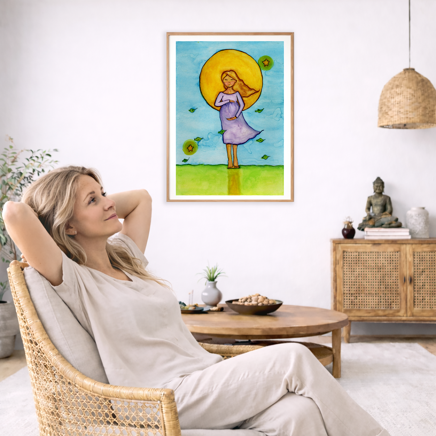Woman standing in meditation under a glowing sun with blue sky background, calming watercolor spiritual illustration.  The poster is framed and is in the center of the living room wall. To the left a woman is relaxing in her chair with her hands behind her head. There is a small coffee table beside her with a bowl of walnuts, incense and a small green plant. On the right side of the room is a cabinet with a Buddha statue, books and an urn on it. To the left is a green floor plant.
