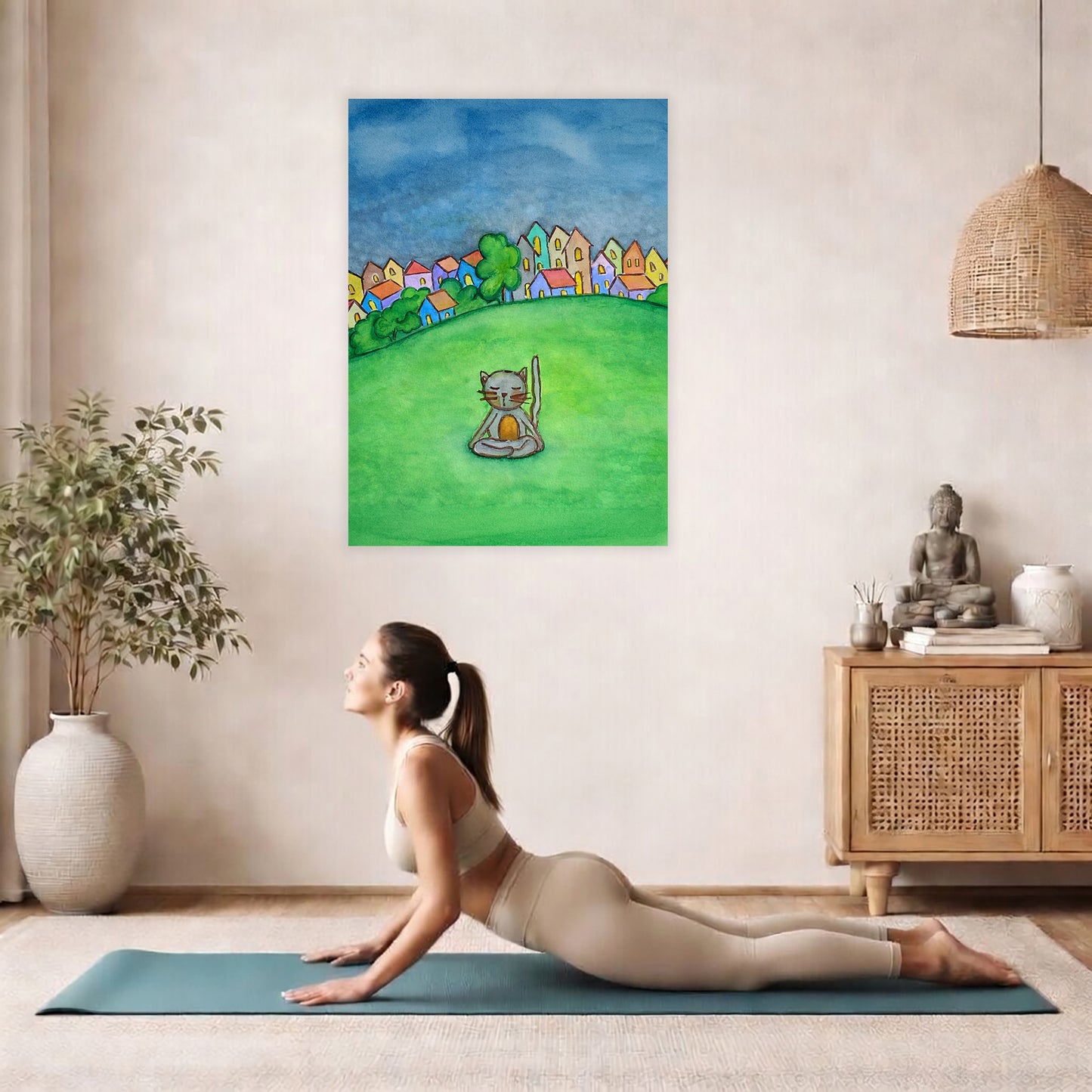 Poster of a gray cat meditating peacefully in a park surrounded by nature. The poster is hanging on the wall. A woman on her yoga mat is doing the cobra pose in front of the poster. here is a potted plant on the left side and a cabinet with a Buddha statue on it on the right side.

