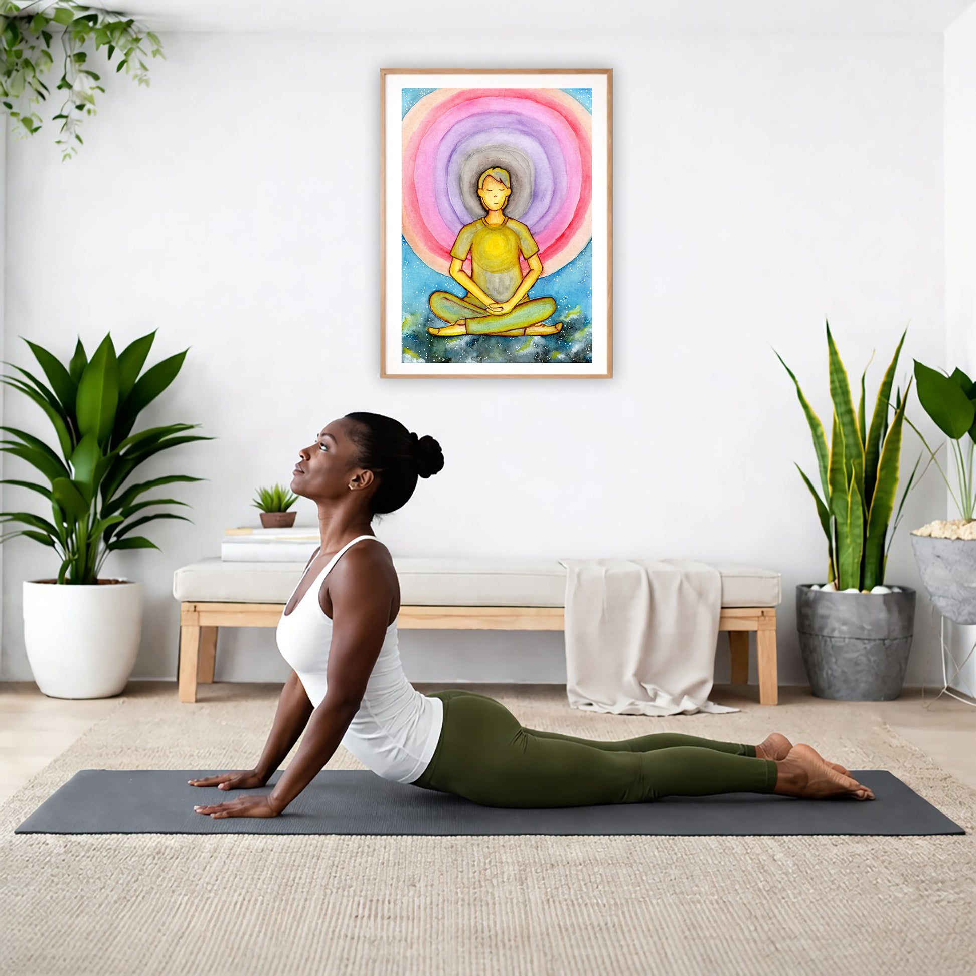 Poster of a young man's heart chakra glowing and aura energy flowing around him.  The poster is hanging on the wall. A woman on her yoga mat is doing the cobra pose in front of the poster. There is a potted plant and a hanging plant on the left side. A padded bench with material draped over it is behind her. On the right side are two potted plants.
