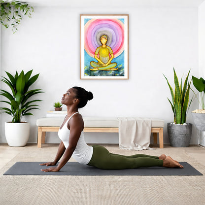 Poster of a young man's heart chakra glowing and aura energy flowing around him.  The poster is hanging on the wall. A woman on her yoga mat is doing the cobra pose in front of the poster. There is a potted plant and a hanging plant on the left side. A padded bench with material draped over it is behind her. On the right side are two potted plants.
