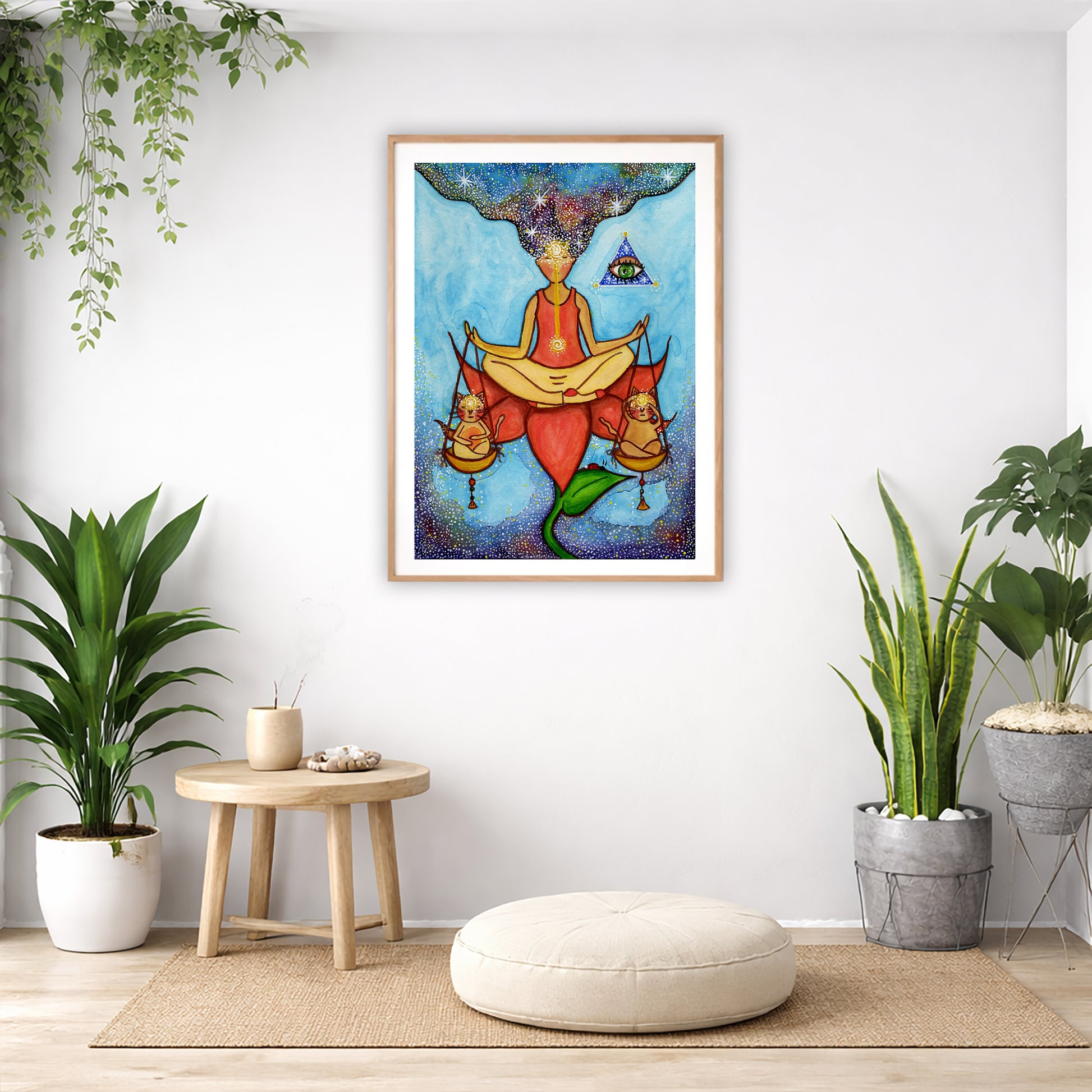Poster of a woman meditating on a lotus with a glowing third eye and holding scales balancing two cats.  The poster is in the center of the living room wall. Below the poster is a pillow on a wicker mat. To the bottom left there is a small table with incense and a bowl of shells. There is also a hanging and potted plant. To the right are two potted green plants.