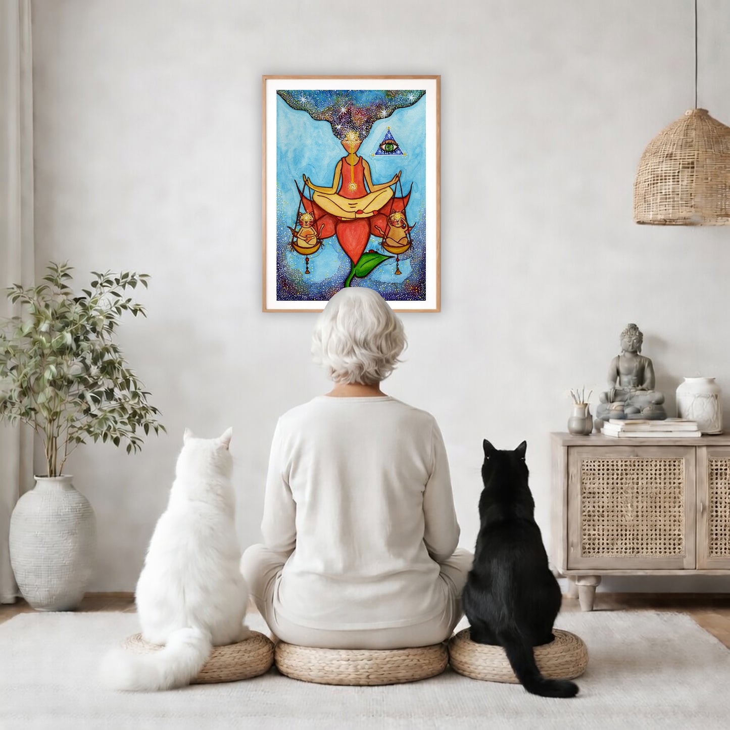 Poster of a woman meditating on a lotus with a glowing third eye and holding scales balancing two cats.  The poster is in the center of the living room wall. A woman is meditating facing the poster with a white cat on her left side and a black cat on her right side. There is a potted plant on the left side and a cabinet with a Buddha statue on it on the right side. 

