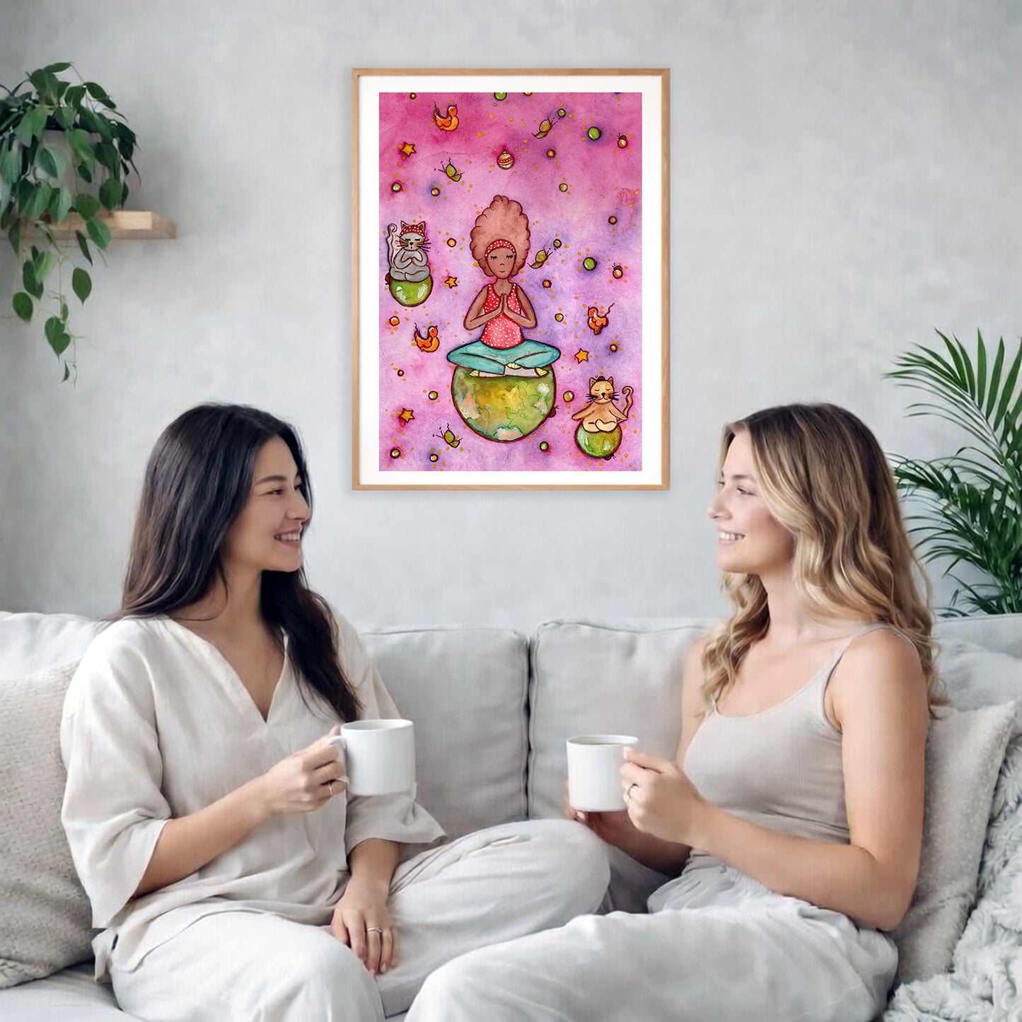 A woman and her cats meditating on the world with a pink background poster. The poster is framed and is in the center of the living room wall. Two female friends are having tea, grapes and cookies on a coffee table in front of the poster. On the left there is a green potted plant and to the right there is a hanging lamp.
