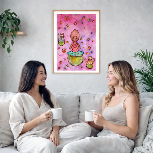A woman and her cats meditating on the world with a pink background poster. The poster is framed and is in the center of the living room wall. Two female friends are having tea, grapes and cookies on a coffee table in front of the poster. On the left there is a green potted plant and to the right there is a hanging lamp.
