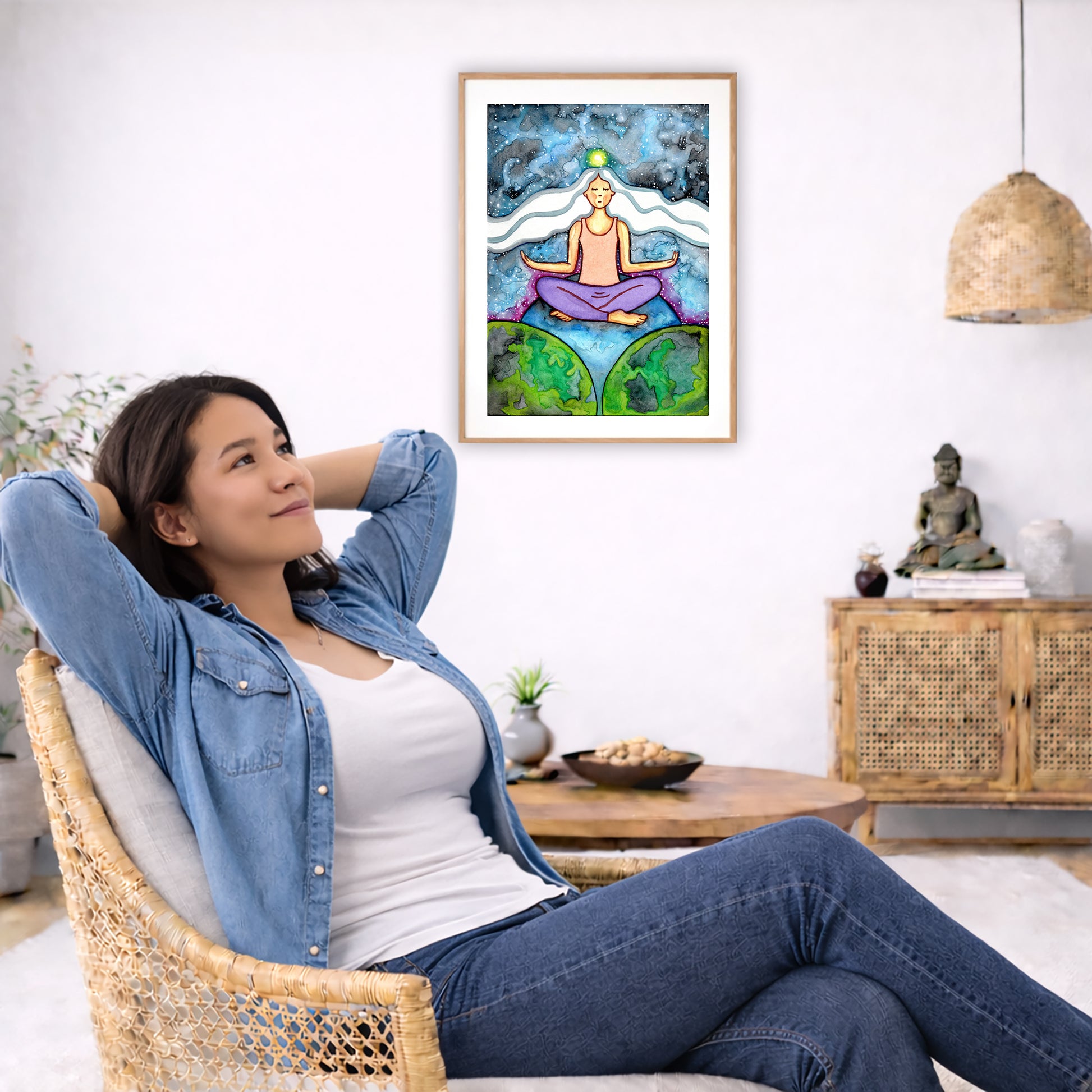 Poster of a woman meditating on three worlds with her crown chakra glowing.  The poster is in the center of the living room wall. To the left a woman is relaxing in her chair with her hands behind her head. There is a small coffee table beside her with a bowl of walnuts, incense and a small green plant. On the right side of the room is a cabinet with a Buddha statue, books and an urn on it. To the left is a green floor plant.
