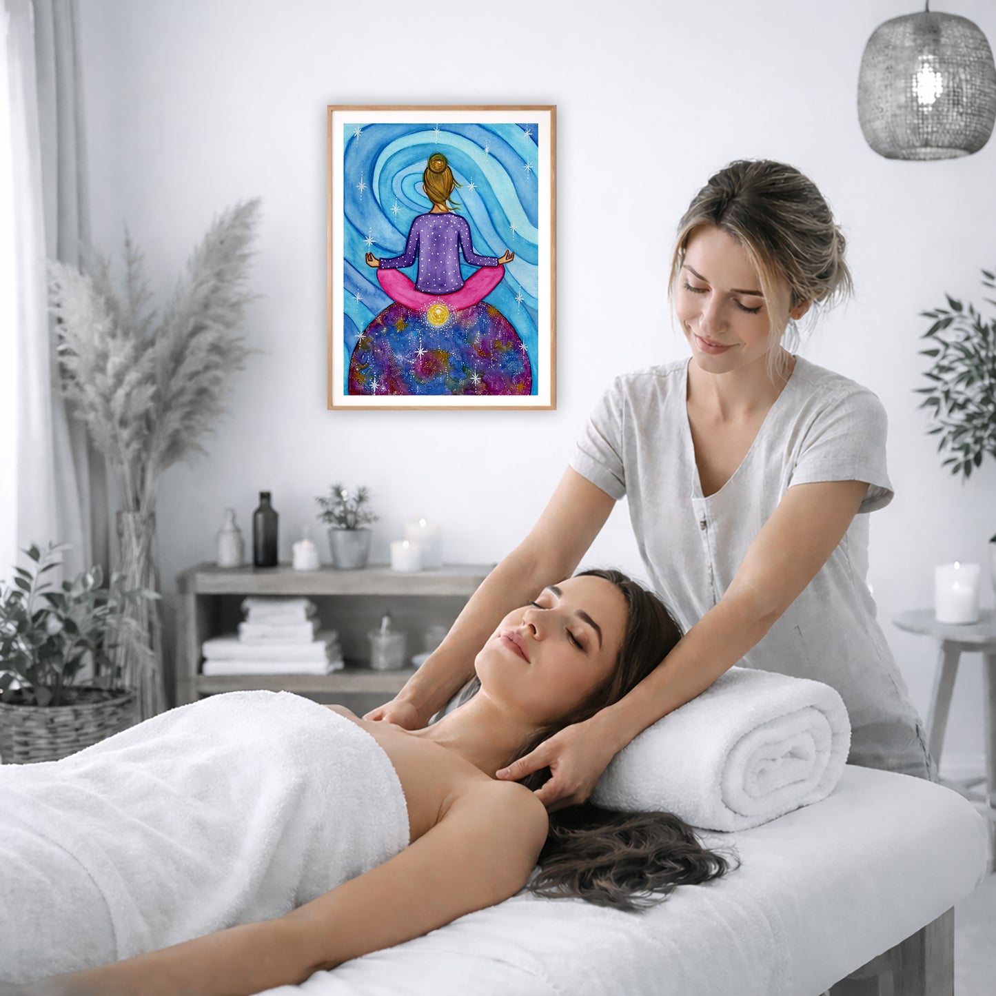 Poster of a woman meditating with her root chakra glowing.  The poster is on the wall of the office of a massage therapist. The therapist is giving her female client a massage. The client is lying face up on a massage table wearing a white towel. To the left is a window, floor plant and large vase of dry flora. A shelf is underneath the poster with candles burning. There is a candle burning on a small table and a hanging lamp with a wicker shade on the right side.