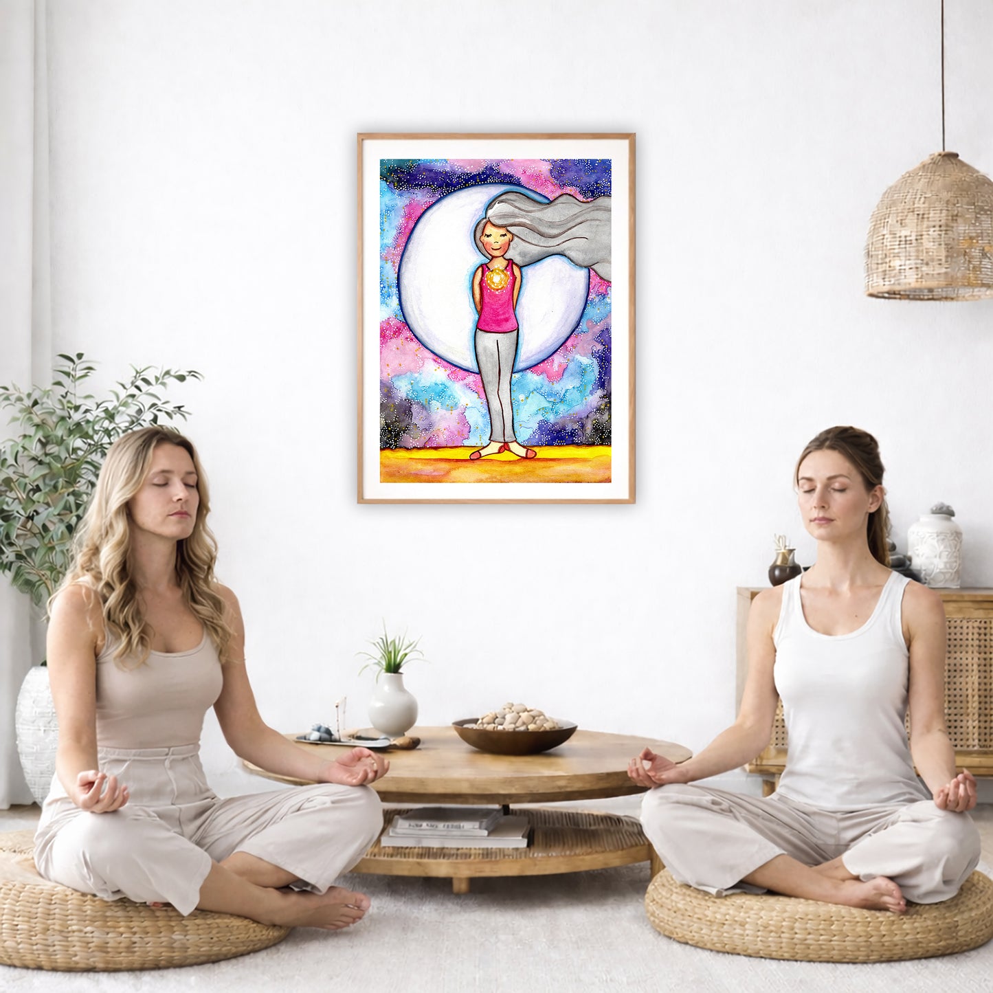 Poster of a woman's heart chakra glowing with love energy. The poster is in the center of the living room wall. Two women are sitting on wicker pillows meditating. Behind them is a small round coffee table with incense, a green potted plant and a bowl of shells. There is a potted plant to the left and a Buddha statue and a vase to the right. 