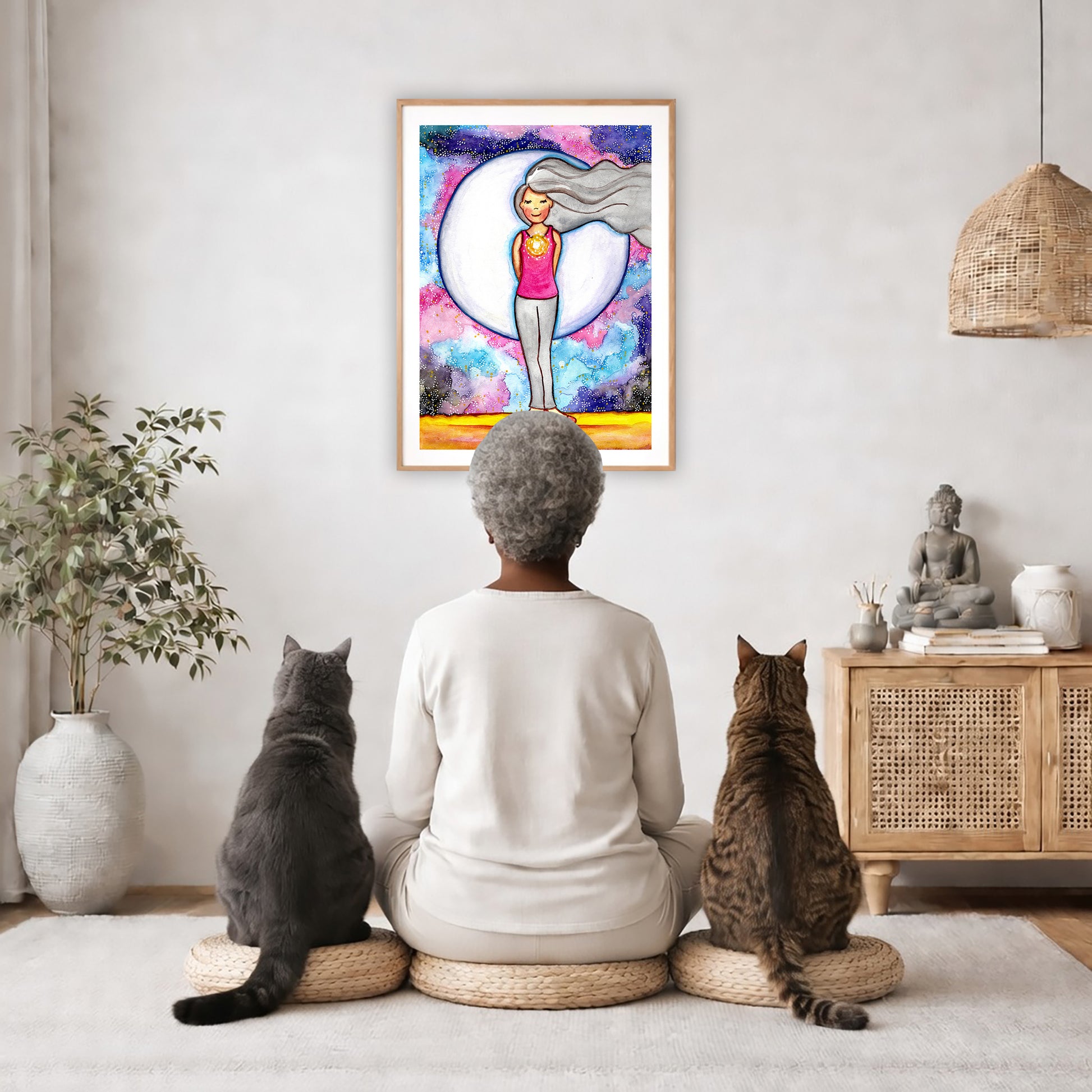 Poster of a woman's heart chakra glowing with love energy.  The poster is in the center of the living room wall. A woman is meditating facing the poster with a white cat on her left side and a black cat on her right side. There is a potted plant on the left side and a cabinet with a Buddha statue on it on the right side. 
