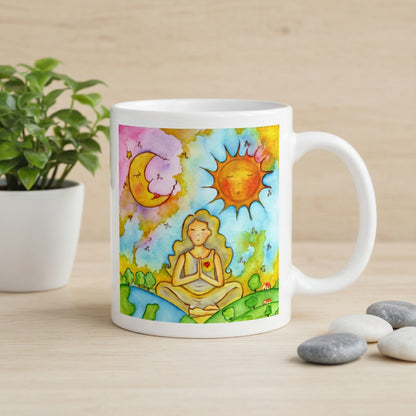 Woman in meditation with sun and moon cosmic design on mug.  Beside the mug are meditation stones. Behind the mug is a green potted plant.
