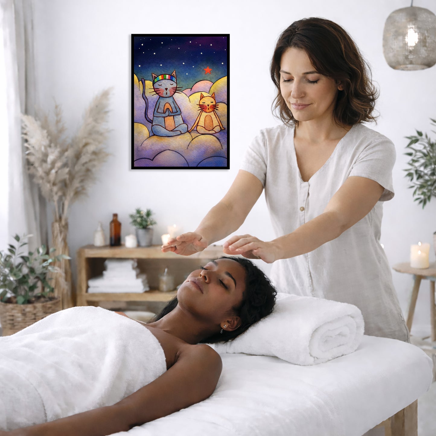 Two cats meditating on a cloud at night under the stars framed poster. This is a print of the original illustration by Brazilian artist Thaís Suizo. The poster is on the wall of the office of a reiki master. The master is giving her client a massage. The client is lying face up on a massage table wearing a white towel. To the left is a window, floor plant and vase of dry flora. There is a shelf underneath the poster with candles burning. On the right side there is a candle burning and a lamp hanging.