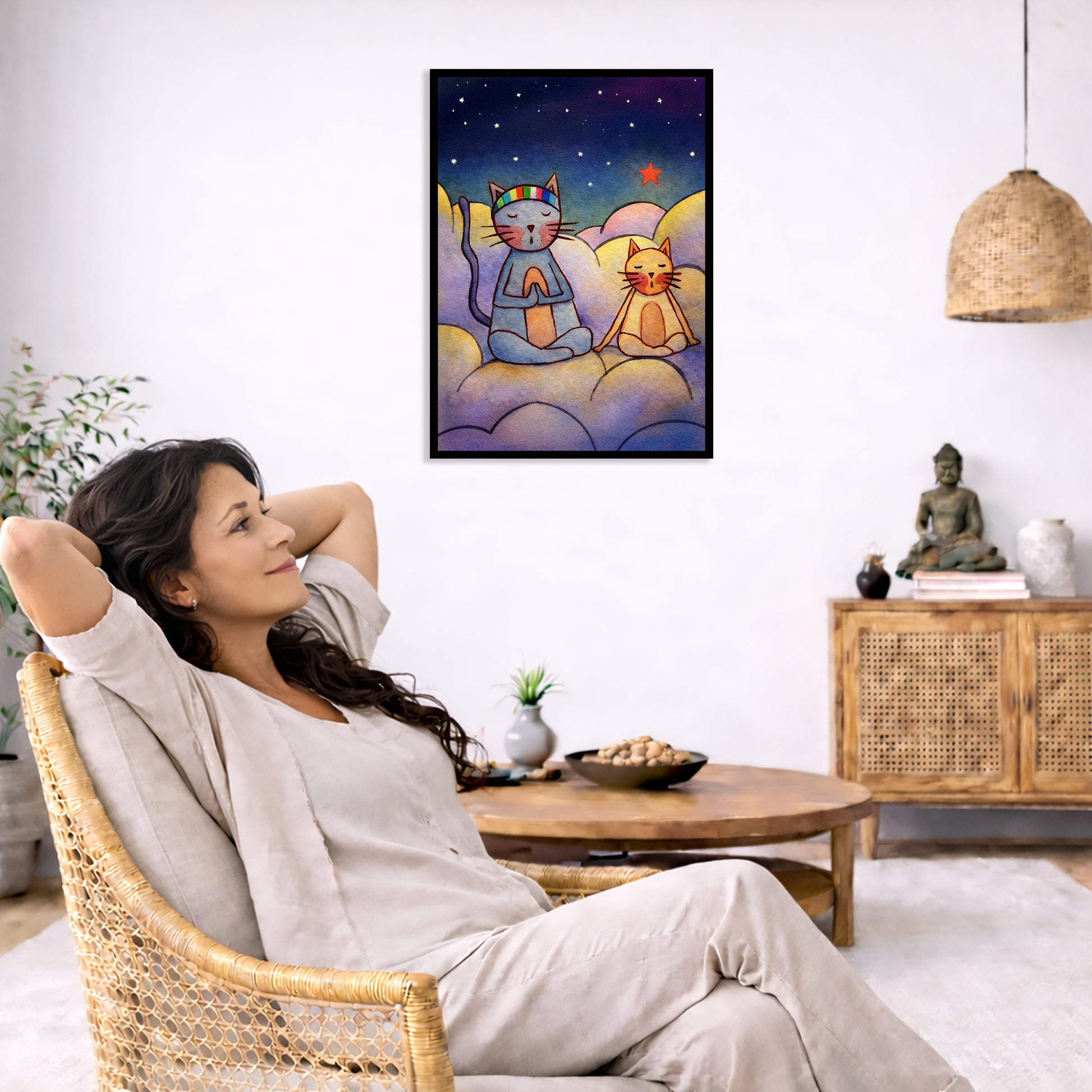 Two cats meditating on a cloud at night under the stars framed poster. This is a print of the original illustration by Brazilian artist Thaís Suizo. The poster is in the center of the living room wall. To the left a woman is relaxing in her chair with her hands behind her head. There is a small coffee table beside her with a bowl of walnuts, incense and a small green plant. On the right side of the room is a cabinet with a Buddha statue, books and an urn on it. To the left is a green floor plant.