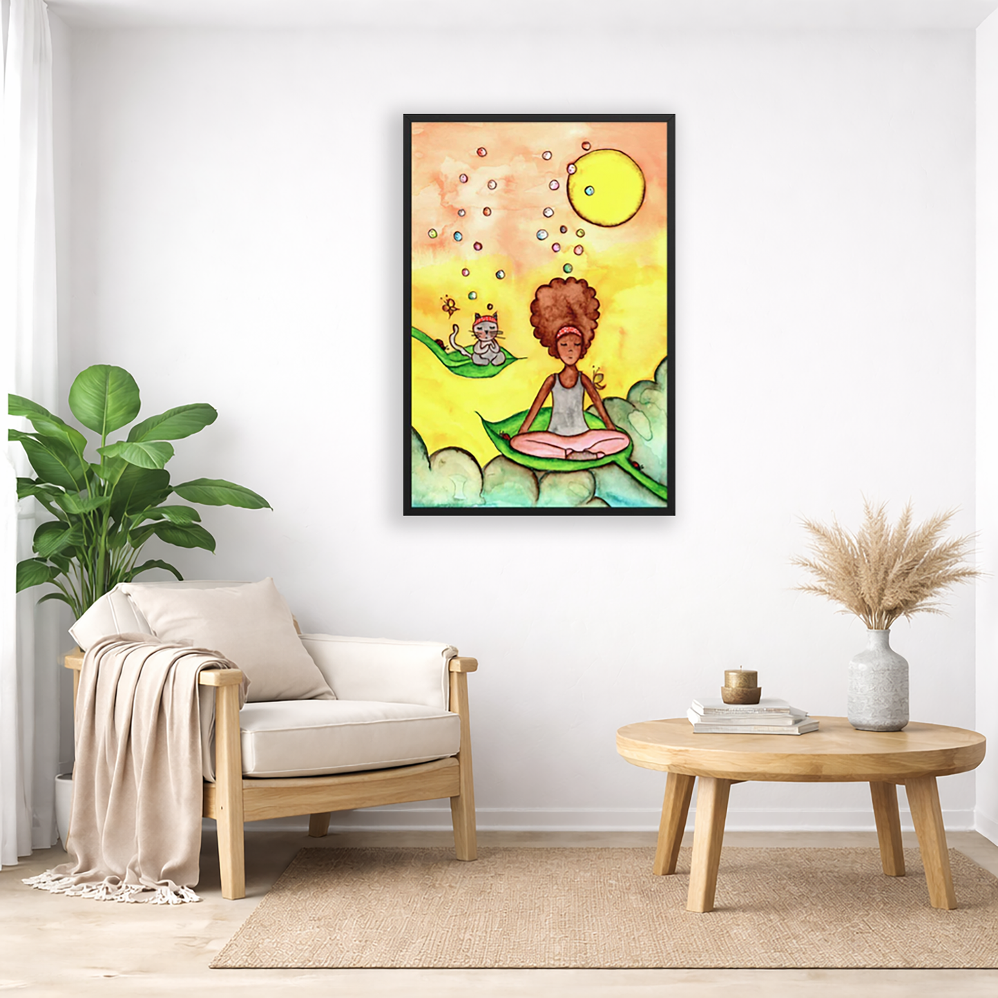 Poster of a woman and her cat sitting on leaves meditating with a yellow sunny joyful background.  The poster is framed and is in the center of the living room wall. Below the poster to the left is a living room chair, a floor plant and white curtains. To the right is a small table with books, a candle and a vase with dry flora.