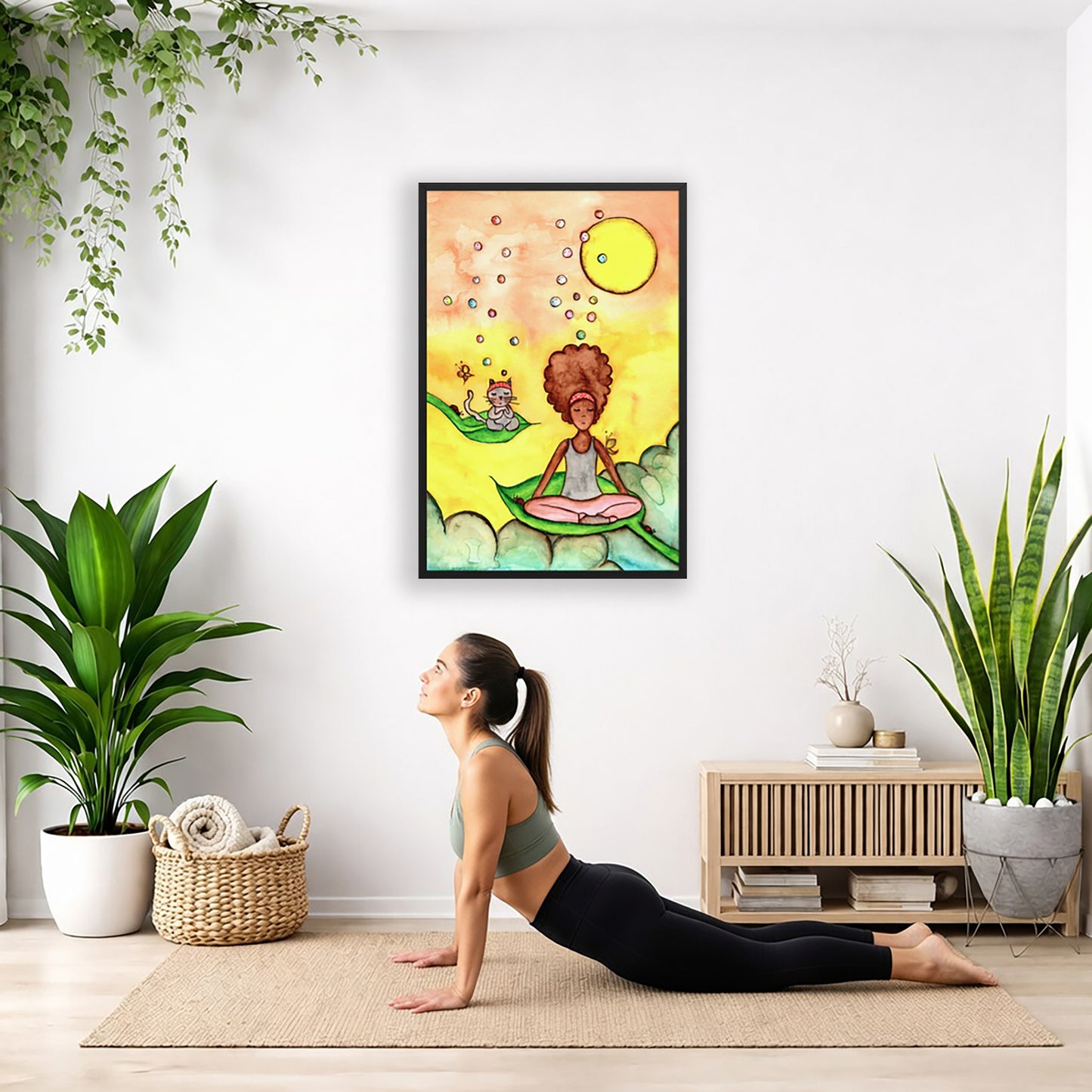 Poster of a woman and her cat sitting on leaves meditating with a yellow sunny joyful background.  The poster is hanging on the wall. A woman on her yoga mat is doing the cobra pose in front of the poster. There is a potted plant, a hanging plant and a basket of cloth material on the left side. On the right side of her is a small cabinet books and a dry plant. There is also a floor plant on the right side.