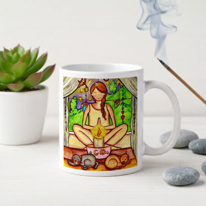 Candlelight trataka meditation design on mindfulness mug. Two cats are sleeping in front of the lady as she meditates.  The mug is on a counter. Beside the mug are meditation stones. Behind the mug is a green potted plant.