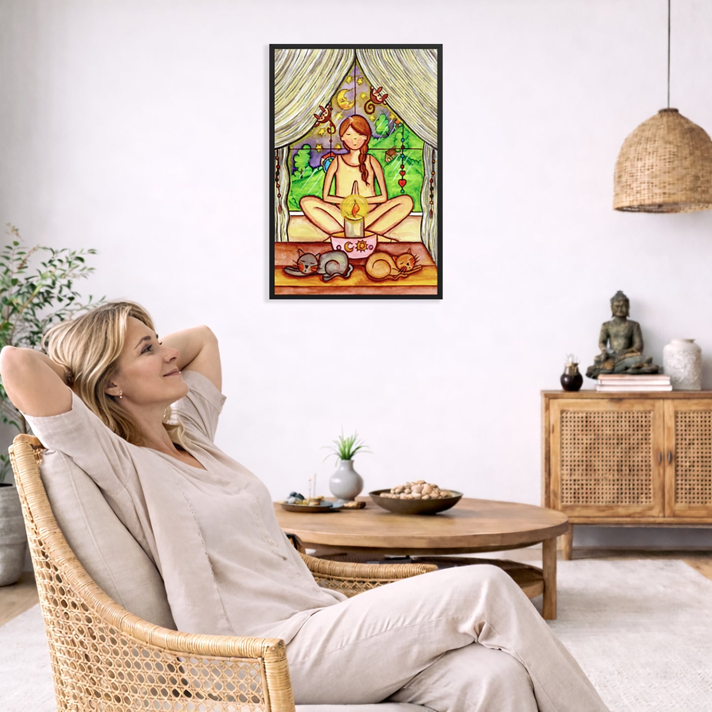 Woman mediating on candlelight framed poster. This is a print of the original hand-painted watercolor by Brazilian artist Thaís Suizo for the LET'S MEDITATE SERIES of mediation guides.  The poster is in the center of the living room wall. To the left a woman is relaxing in her chair with her hands behind her head. There is a small coffee table beside her with a bowl of walnuts, incense and a small green plant. On the right side of the room is a cabinet with a Buddha statue, books and an urn on it. 