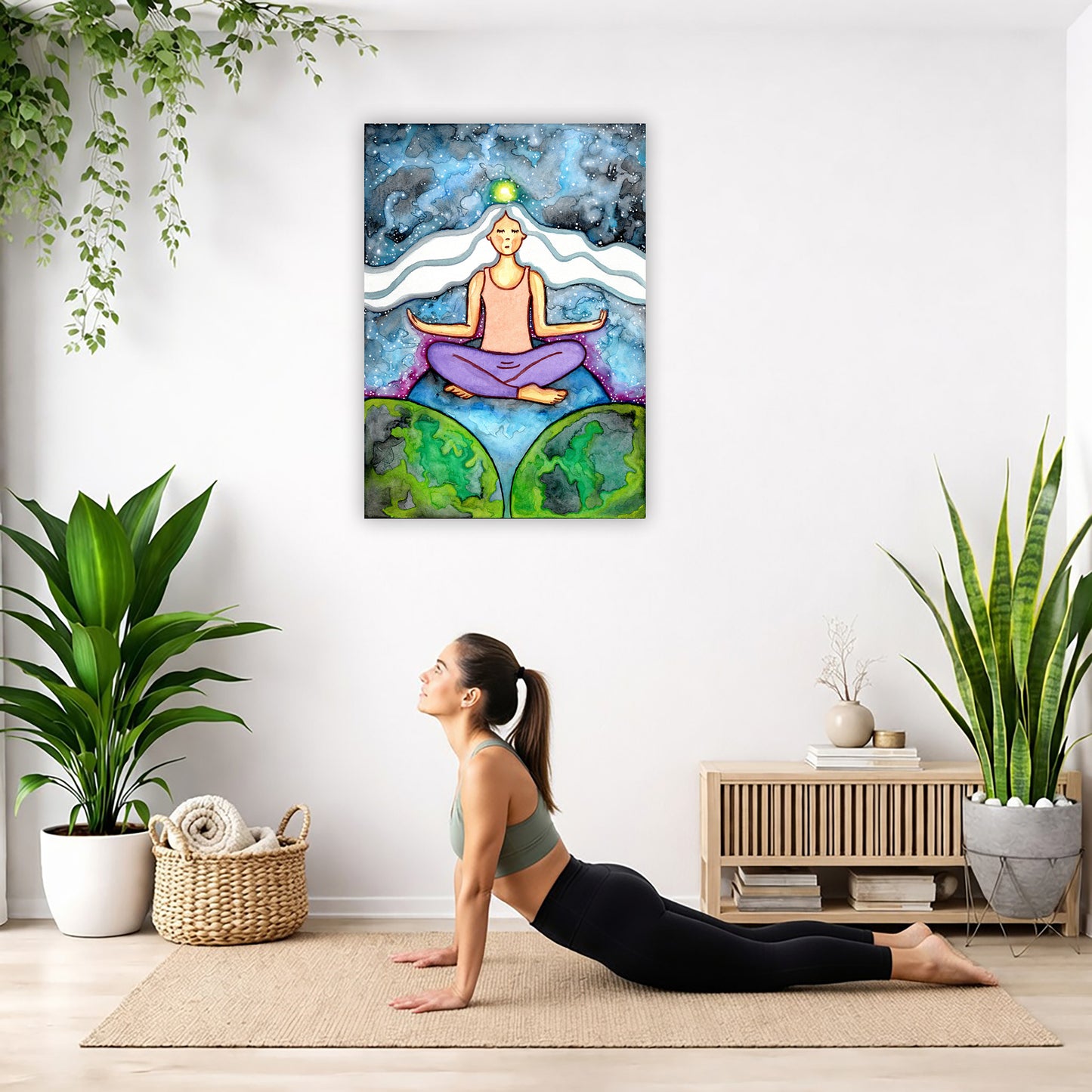 Woman with crown chakra glowing canvas poster. She is sitting on top of the world.  The poster is hanging on the wall. A woman on her yoga mat is doing the cobra pose in front of the poster. There is a potted plant and a hanging plant on the left side. A padded bench with material draped over it is behind her. On the right side are two potted plants.
