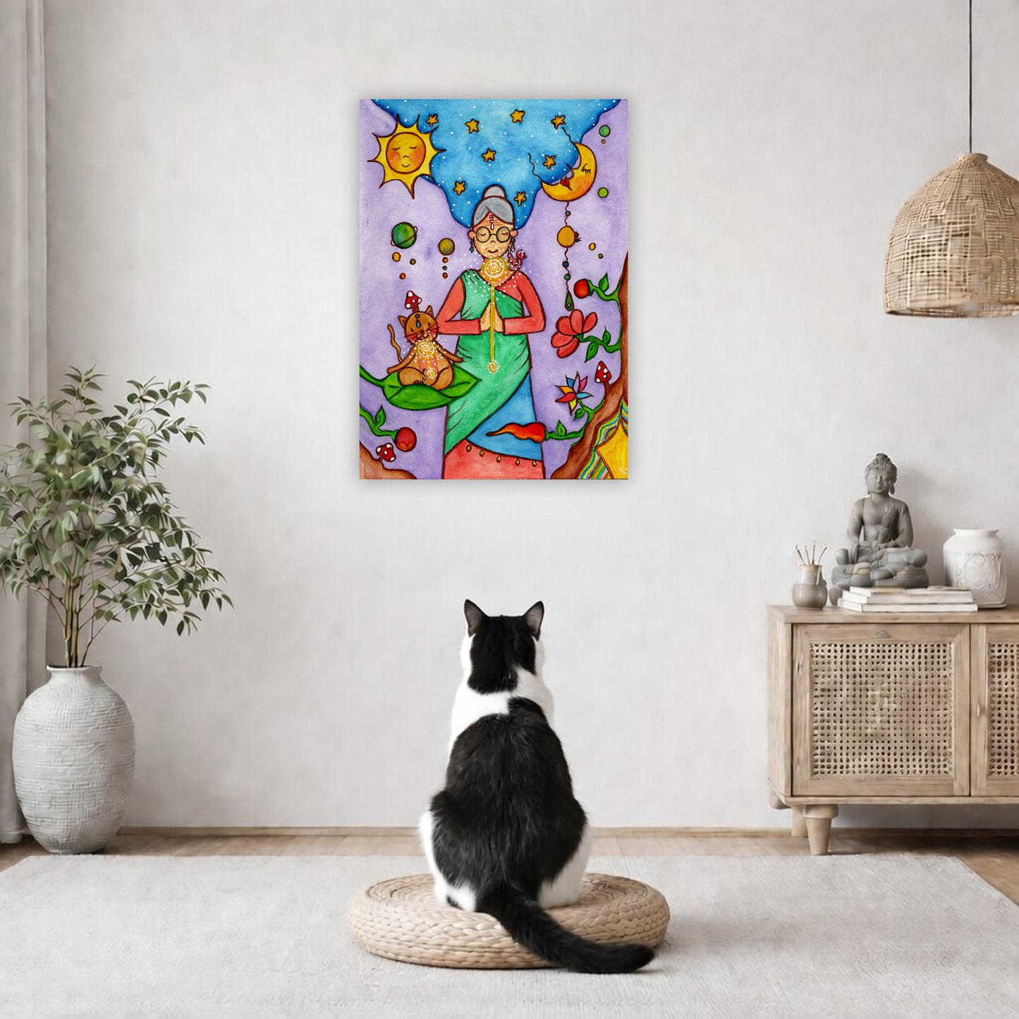 Throat chakra canvas print of a woman and her cat meditating under the sun and the moon.  The poster is in the center of the living room wall. A black and white cat is staring at the poster. There is a potted plant on the left side and a cabinet with a Buddha statue on it on the right side. 
