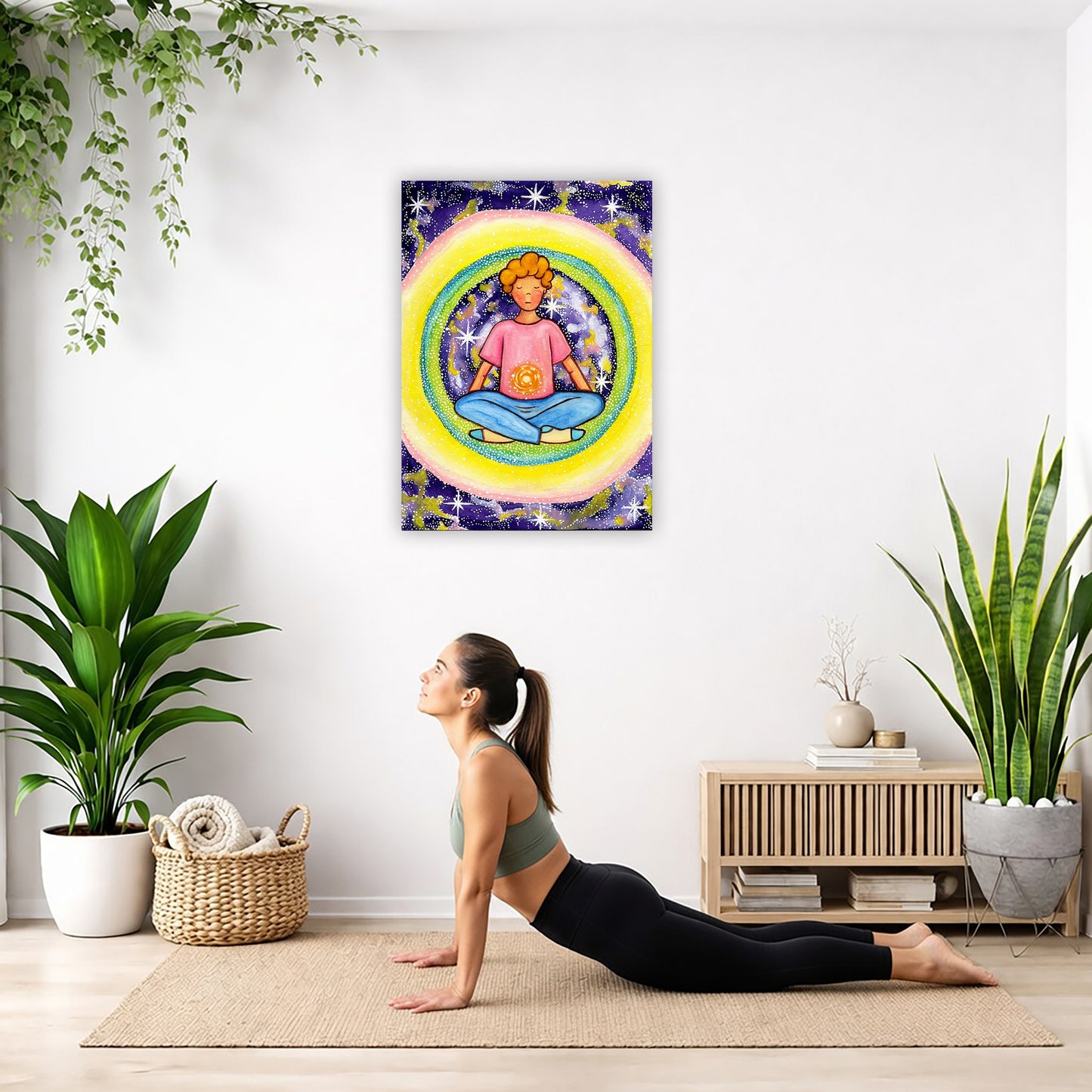 Young man meditating with his solar plexus glowing canvas. Surrounding him is his colorful aura. This is a print of the original hand-painted watercolor by artist Thaís Suizo for the LET'S MEDITATE SERIES of mediation guides.  The poster is hanging on the wall. A woman on her yoga mat is doing the cobra pose in front of the poster. There is a potted plant and a hanging plant on the left side. A padded bench with material draped over it is behind her. On the right side are two potted plants.
