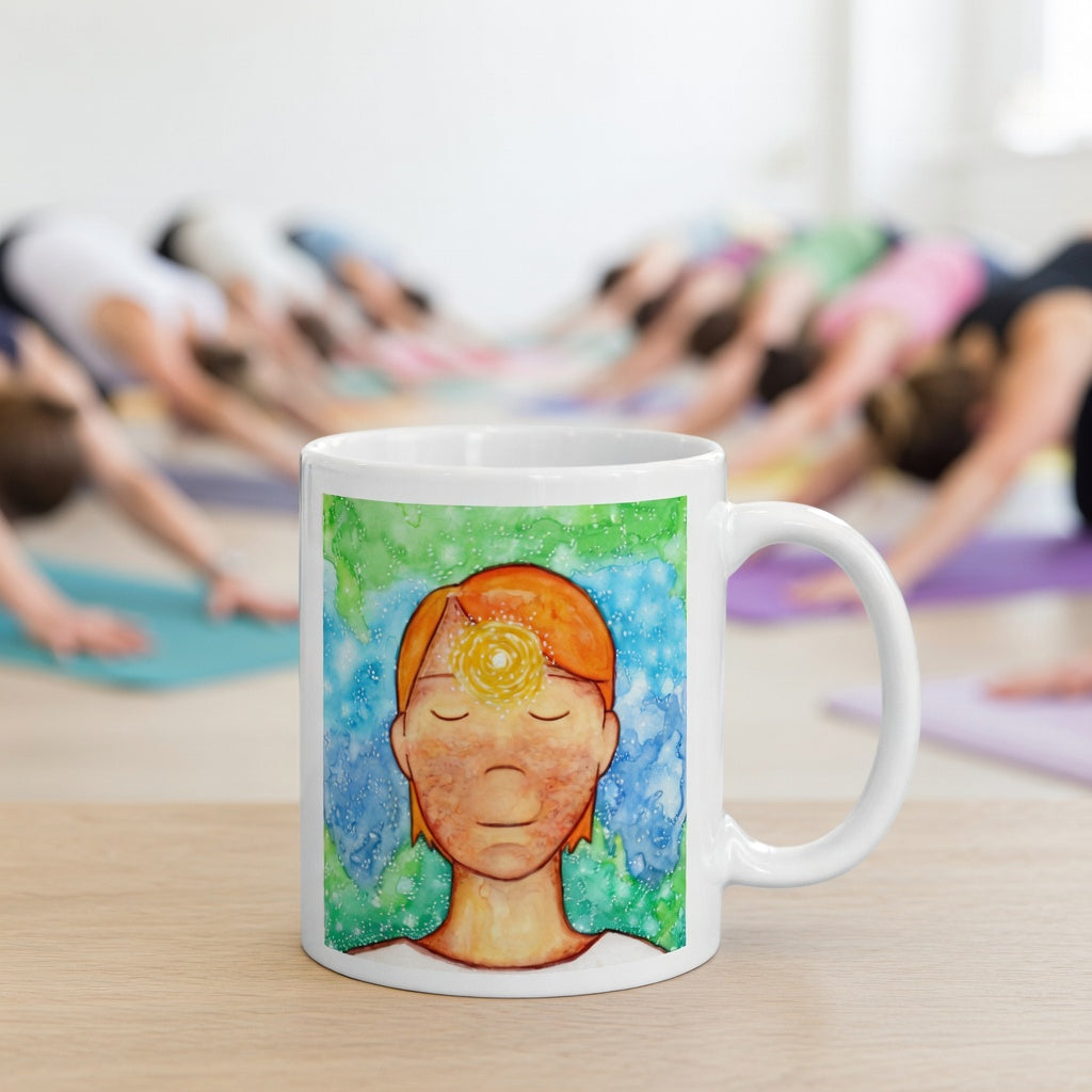 Man meditating with glowing third eye chakra on forehead, symbolizing intuition, awareness and inner vision, spiritual chakra artwork on a meditation themed coffee mug. The mug is in front of a yoga class doing the downward facing dog posture.