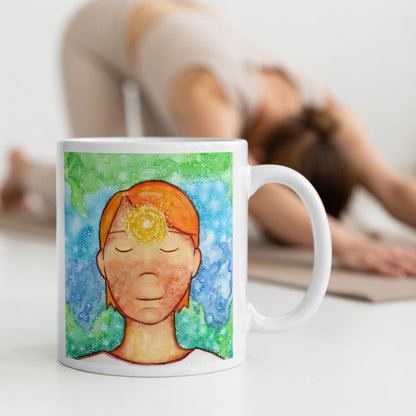 Man meditating with glowing third eye chakra on forehead, symbolizing intuition, awareness and inner vision, spiritual chakra artwork on a meditation themed coffee mug.  The mug is in front of a woman doing the yoga posture downward facing dog.