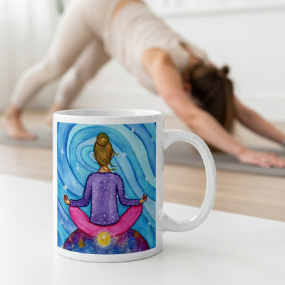 Meditating figure with glowing root chakra at base of spine, symbolizing grounding, stability and security, chakra energy artwork on a coffee mug.  The mug is in front of a woman doing the yoga posture downward facing dog.
