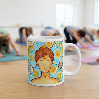 Man meditating with glowing throat, brow and crown chakras, symbolizing communication, intuition and spiritual connection, chakra artwork on a coffee mug. The mug is in front of a yoga class doing the downward facing dog posture.