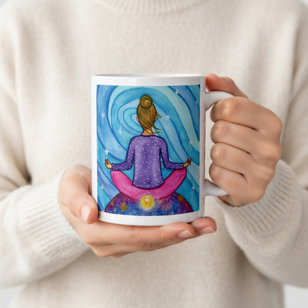Meditating figure with glowing root chakra at base of spine, symbolizing grounding, stability and security, chakra energy artwork on a coffee mug. The hands of a person wearing a white sweater are holding the mug up to display the design.