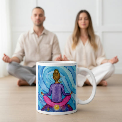 Meditating figure with glowing root chakra at base of spine, symbolizing grounding, stability and security, chakra energy artwork on a coffee mug.  A large mug is at the bottom front displaying the design. There is a couple meditating in the background.