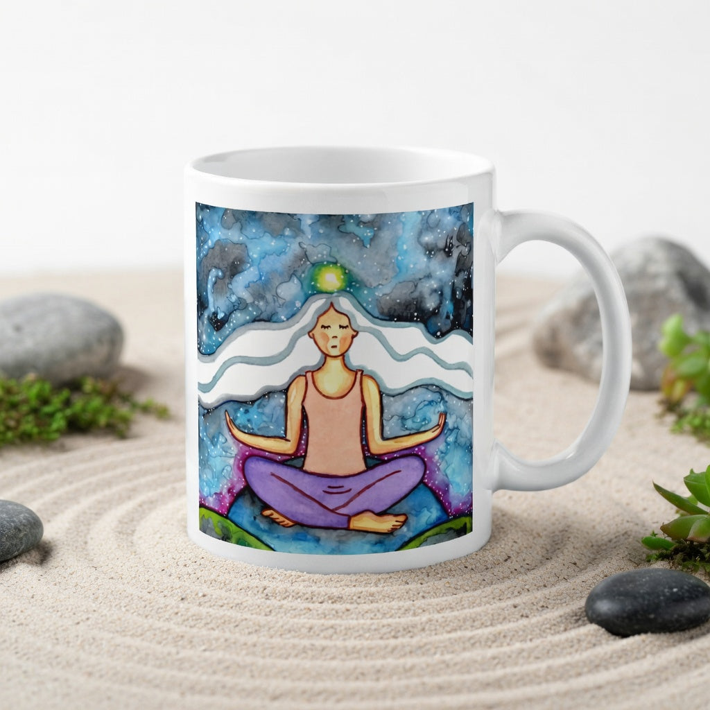 Meditating figure with glowing crown chakra at top of head, symbolizing higher consciousness and spiritual connection, chakra artwork featured on a mindfulness mug.  The mug is in a beautifully raked zen garden with bushes, rocks and plants behind it.